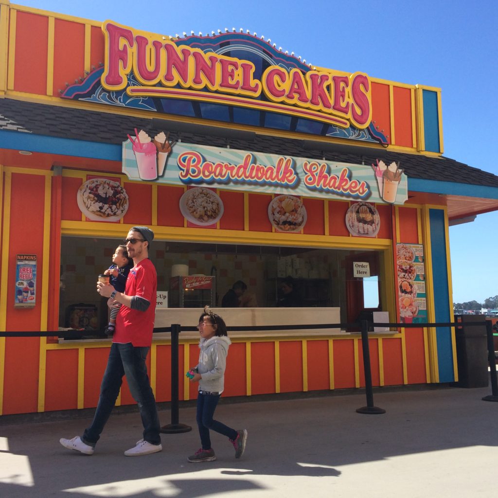 a man and two girls walking by a funnel cake stand at the Santa Cruz Beach Boardwalk in Santa Cruz, California