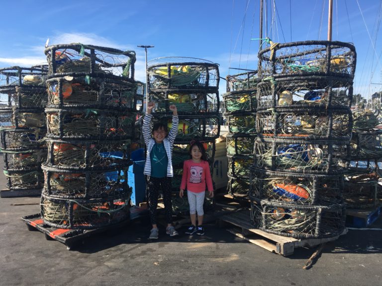 two girls standing between stacks of crab traps at Pillar Point Harbor in Half Moon Bay, California