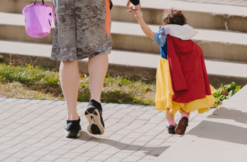 Little girl dressed in a snow white costume holding her dads hand at Disneyland