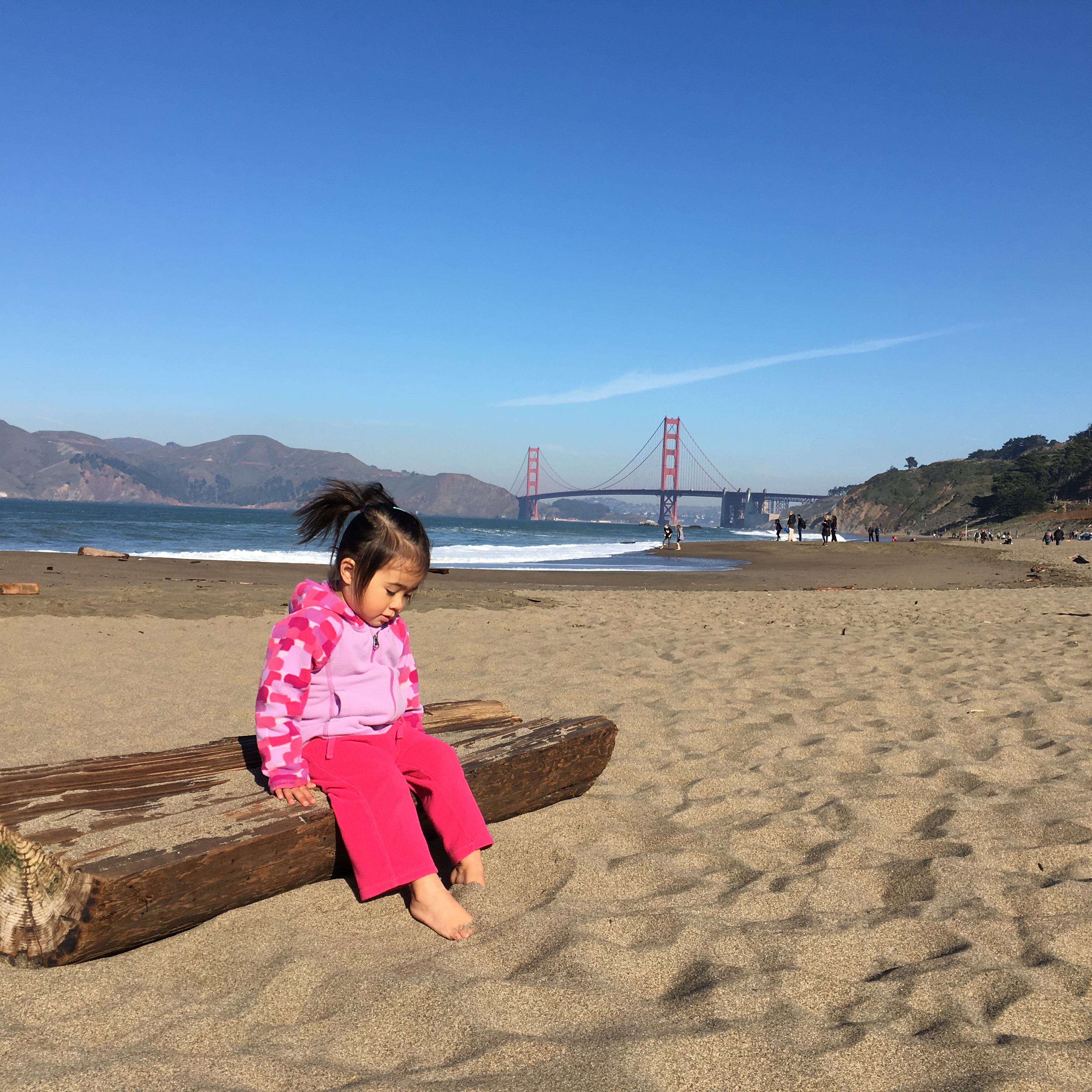 little girl sitting on a log at Baker Beach with the Golden Gate Bridge in the background