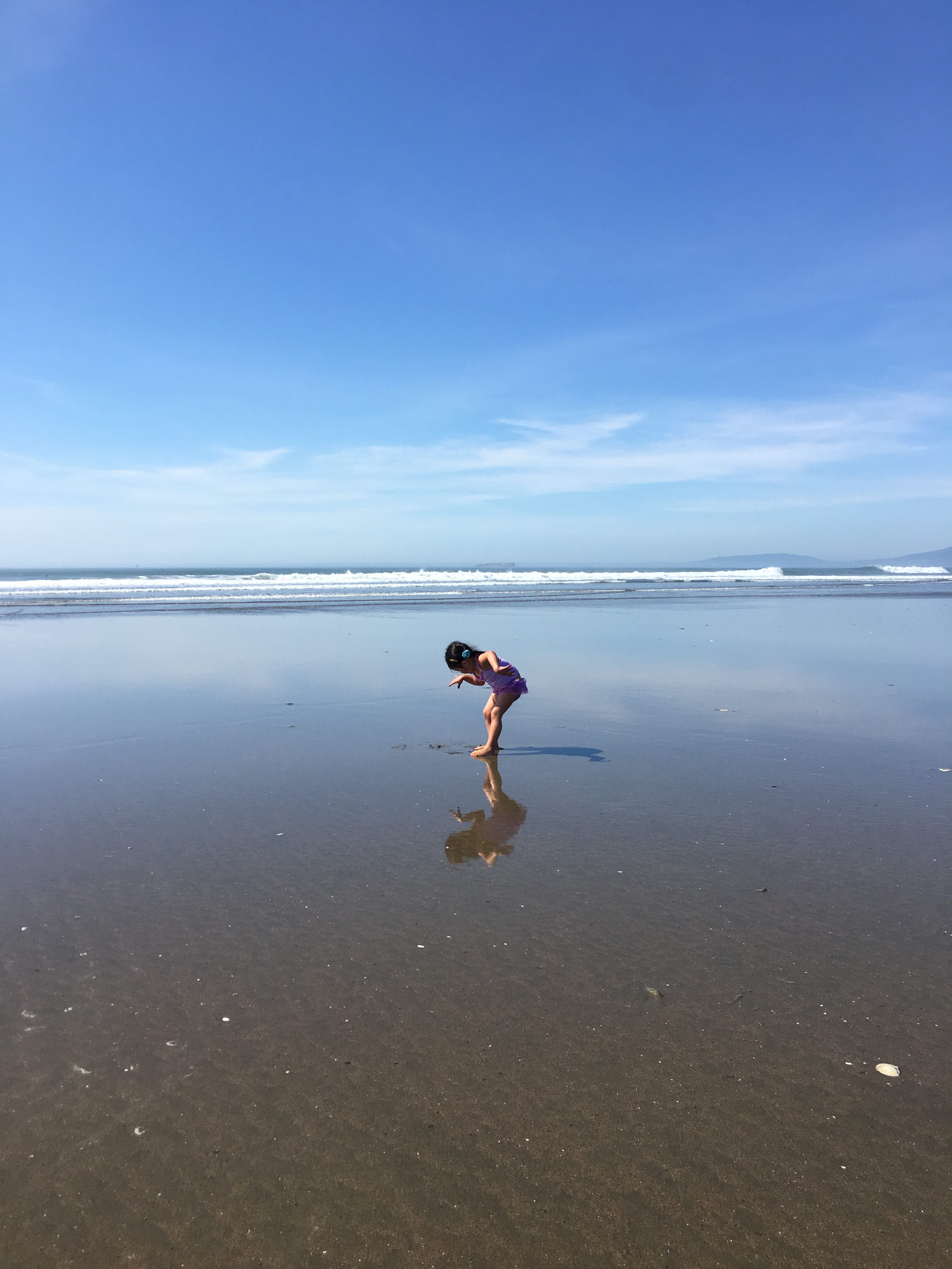 little girl looking at her reflection in the water at Ocean Beach San Francisco