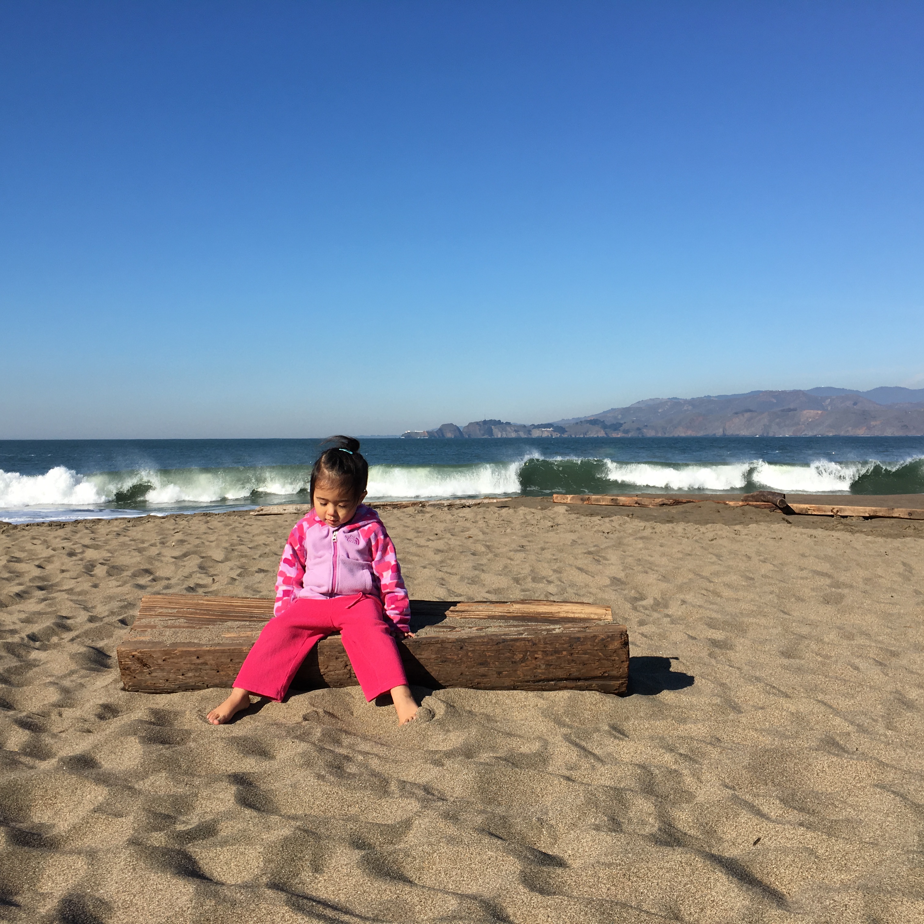 girl sitting on a log at Baker Beach San Francisco