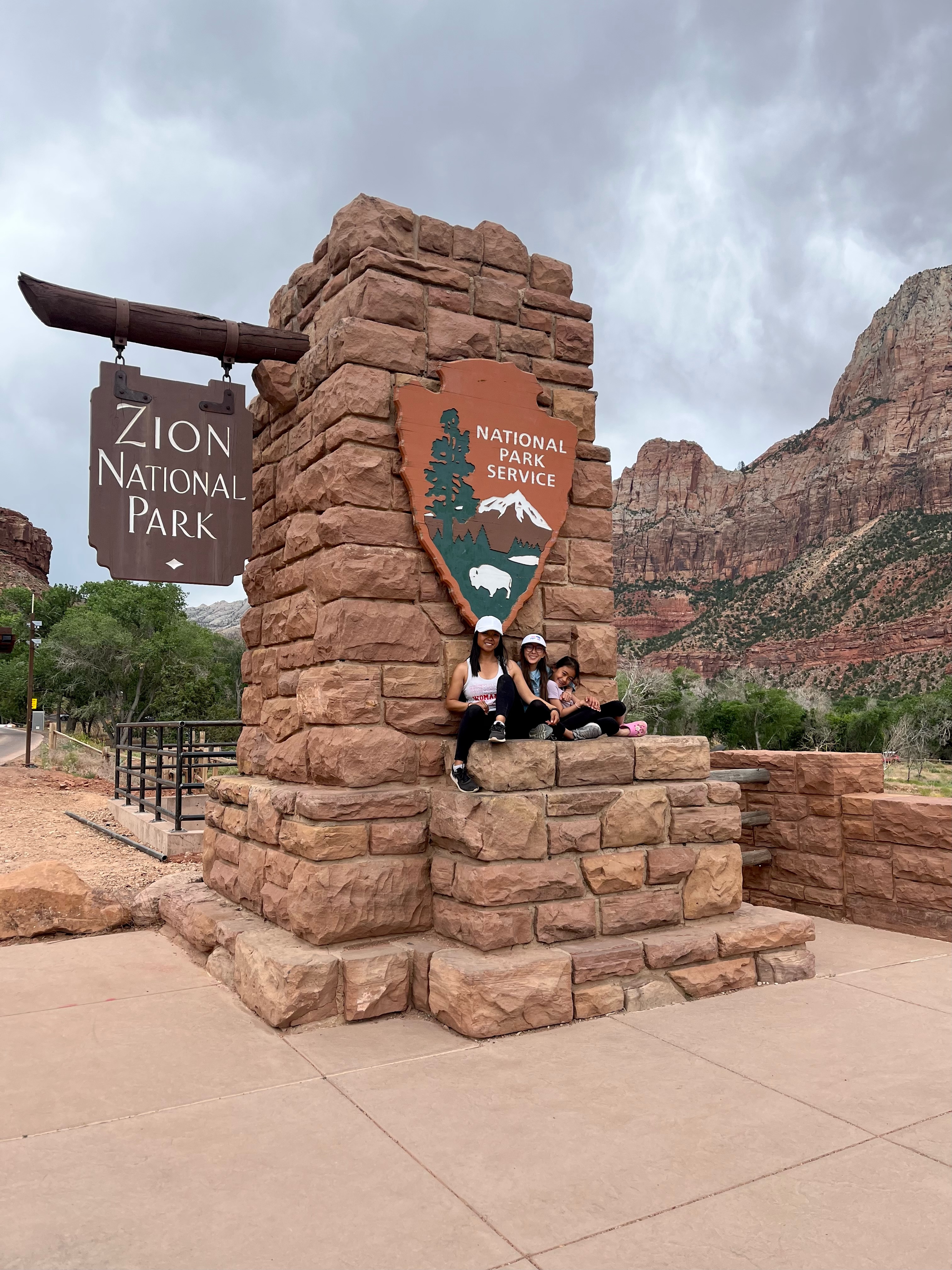 mom and daughters sitting at the entrance of Zion National Park in Utah